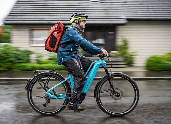 Radfahrer von der Seite aufgenommen auf Pedelec im Regen unterwegs. 